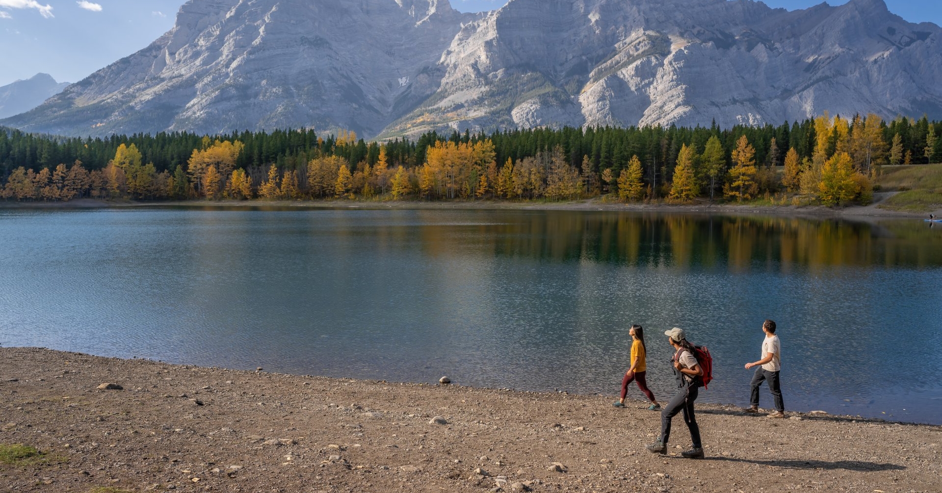 a group walking along a lake gazing out at the larch trees and mountain scenery