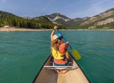 a woman canoeing on Barrier Lake in the summer with blue skies and mountains in the background