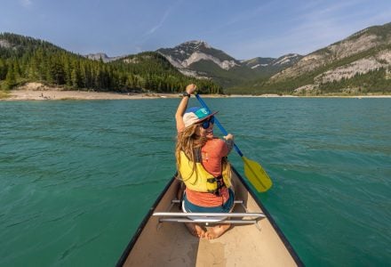 a woman canoeing on Barrier Lake in the summer with blue skies and mountains in the background