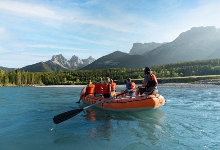 a tour group with Canmore Raft tours floating down the Bow River in the summer with the Three Sisters Mountains in the background