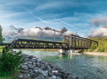 the Canmore Engine Bridge across the Bow River in the summer with mountains in the background