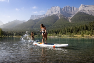 two women stand up paddleboarding and splashing each other on quarry lake in the summer