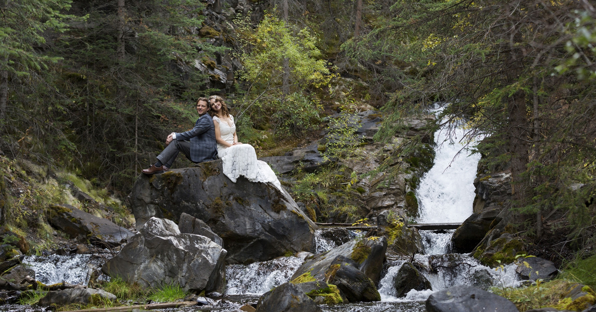 a bridge and groom posing for their wedding photo in front of a waterfall in Kananaskis