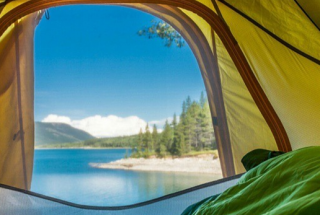 a first person perspective of a camper looking out their tent out into mountain scenery and a lake