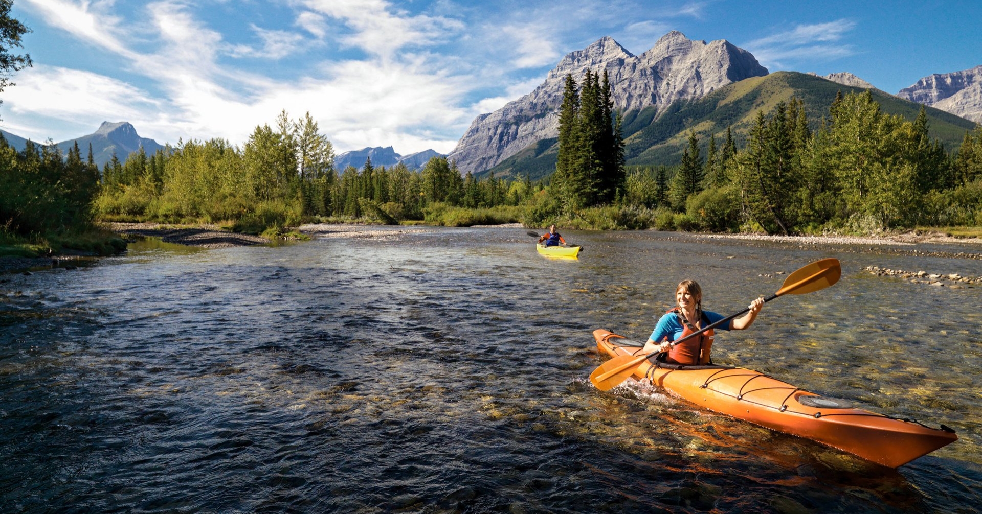 two people kayaking on the Kananaskis River in the summer with mountain ranges in the background