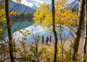 three people standing by a reflective lake gazing out into the mountains on a fall day