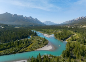 a drone shot of the bow river carving through the town of canmore with mountains on the horizon