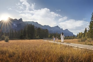 a woman and two children walking along policeman's creek boardwalk in the summer with rundle range in the background