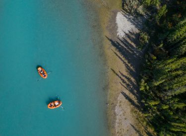a drone shot of two orange rafts floating down the bright blue bow river