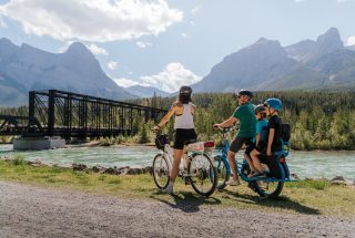 a family biking on the bow river loop trail with the infamous canmore engine bridge in the background