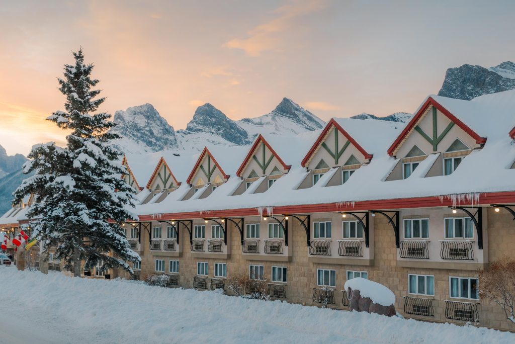 an exterior shot of Canmore Inn & Suites in the winter at sunset with the Three Sisters Mountains in the background