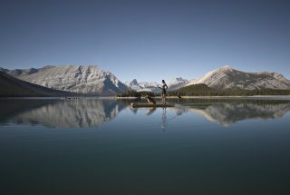 a woman paddleboarding with her dog on the calm waters of Spray Lakes in Kananaskis