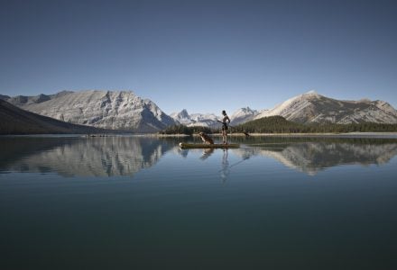 a woman paddleboarding with her dog on the calm waters of Spray Lakes in Kananaskis