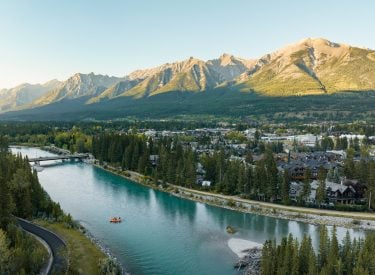 an aerial shot of Canmore with the Bow River cutting through town and mountains in the background