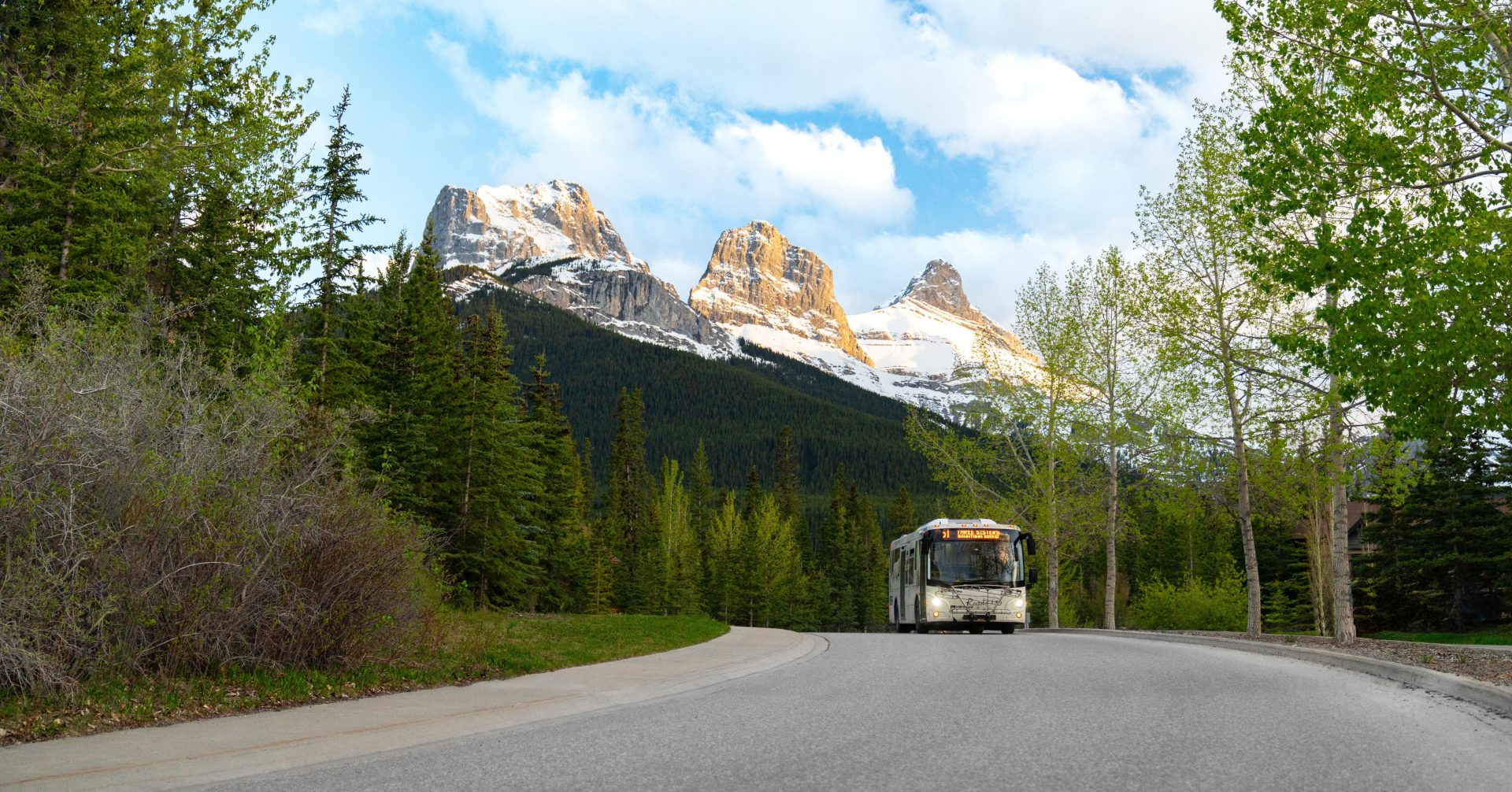 a roam transit bus driving along a road with Three Sisters Mountains in the background