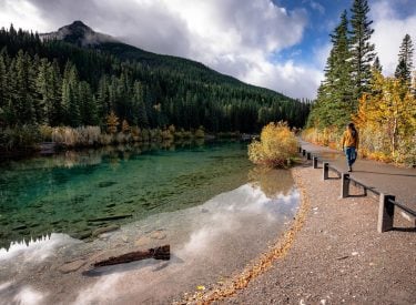 a woman walking on a boardwalk about the water at mount lorette ponds day use area in the fall