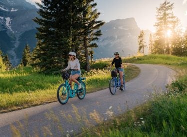 two people biking along Legacy Trail in the summer on Pedego Electric Bike rentals with mountains in the background
