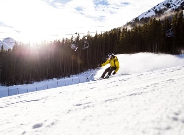 a skier in a yellow jacket skiing down a snowy hill at Nakiska Ski Resort with a chairlift in the background