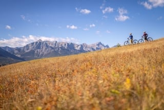 Two people mountain biking on a trail in the fall with mountains in the background