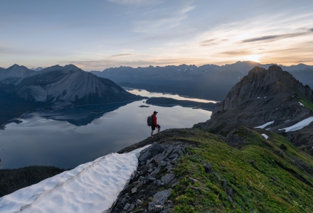 a solo hiker at the peak of a mountain with alpine lakes and mountain ranges in the background. Photo was taken at sunrise