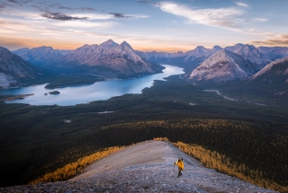 A hiker walking up Tent Ridge with Spray Lake Reservoir in the background at golden hour in the fall.