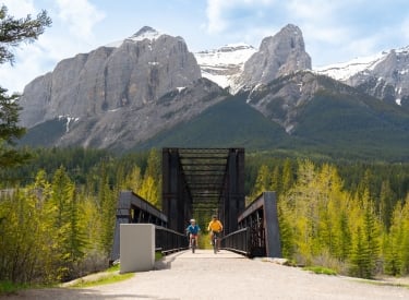 A couple riding their bikes across the Canmore Engine Bridge.