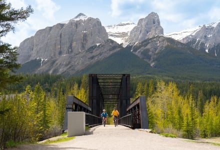 A couple riding their bikes across the Canmore Engine Bridge.