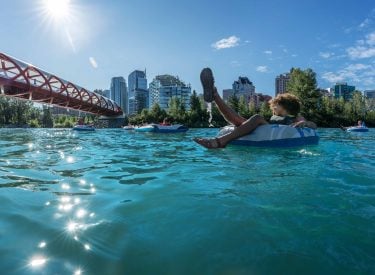 a person floating down the bow river through Calgary with the Peace Bridge in the background
