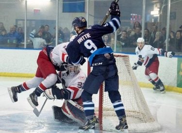 a canmore eagles hockey player tackling an opponent in front of the goal
