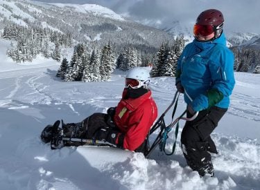 a person assisting another person on an adaptive sled ski