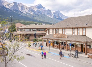 an aerial shot of downtown canmore's Main Street in the summer with people walking in the car-free zone and mountains in the background
