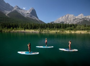 a group stand up paddleboarding on Quarry lake with Ha Ling and Rundle Range in the background