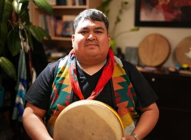 Blackfoot Knowledge Keeper Darcy Turning Robe holding a traditional Indigenous Drum.